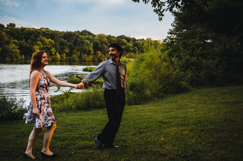 The engaged couple holds hands in front of a lake and trees. I believe couples photography should feel natural.
