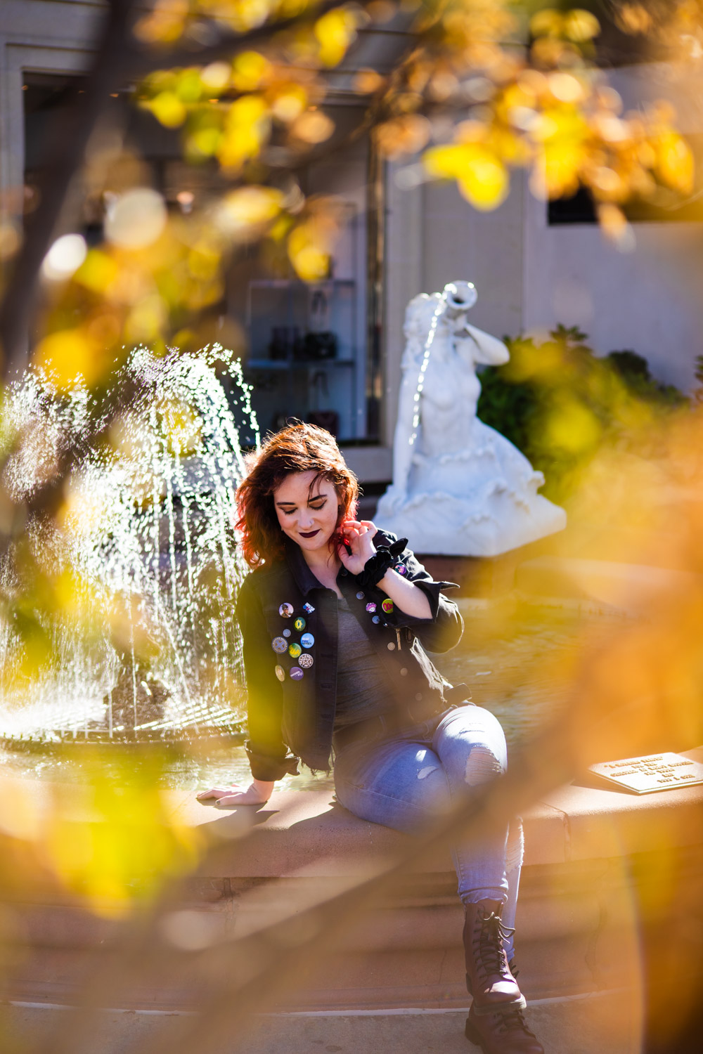 A young adult in punk grunge clothing sits on the edge of a fountain in Kansas City's Plaza district.