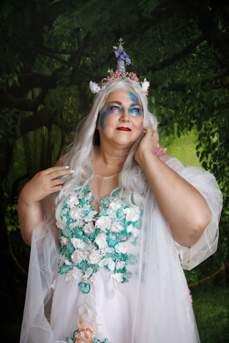 Woman in a fantasy costume and makeup with a unicorn horn in an enchanted forest.