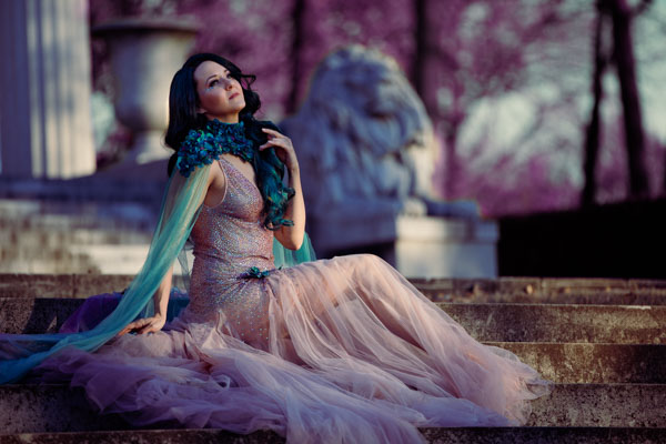 Woman in a sheer rhinestone dress on the steps of an ancient-looking columned building.
