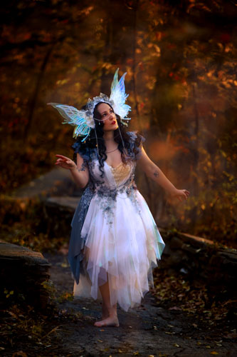 Woman in a white and black fairy costume with wings and winged headdress in the autumn forest.