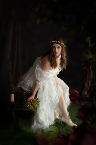 Fine art photograph with painted embellishments of a woman in a white lace dress and delicate pink floral headdress holding a bouquet of withered flowers and looking about to run.