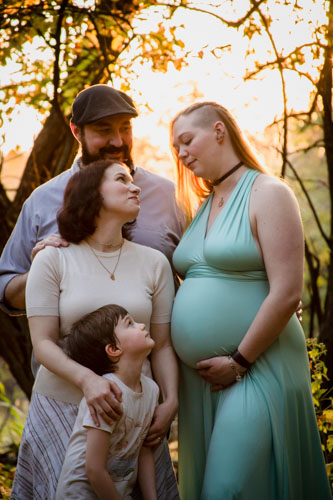 A polyamorous family looks with a pregnant woman look at each other lovingly with trees in the background
