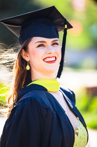 A beautiful woman in a graduation cap and gown smiles proudly