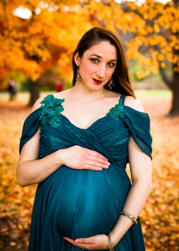 A pregnant woman in an elegant teal dress holds her belly