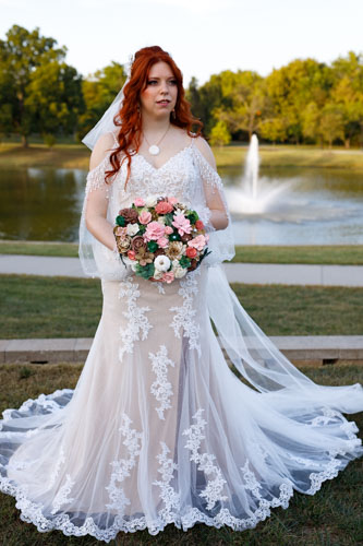 Bride in gown holding flowers and stand in front of a fountain