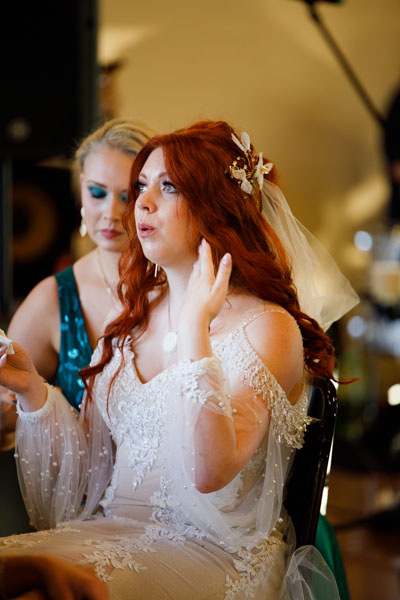 A woman in a beaded wedding dress holds back tears while her maid of honor sits by her