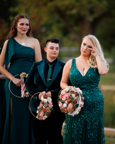 The bridal party holds flowers and wipes away tears as they watch the wedding ceremony
