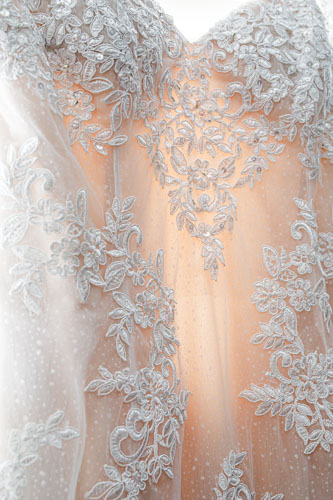 A closeup of the lace and sequin details of a hanging wedding gown